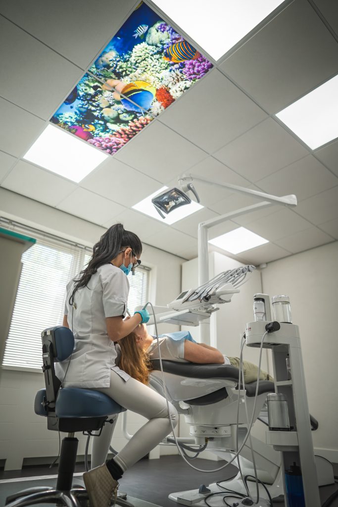 Tandartsbehandeling waarbij een vrouwelijke patiënt in de behandelstoel ligt en de tandarts haar gebit aan het reinigen is.